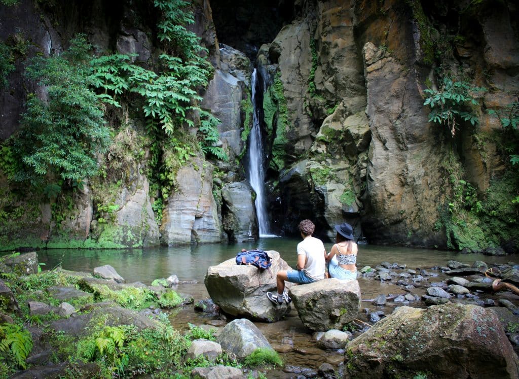 Couple sitting on a rock observing a waterfall in the forest