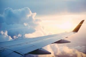 Sun peaking through clouds with a plane wing in sky