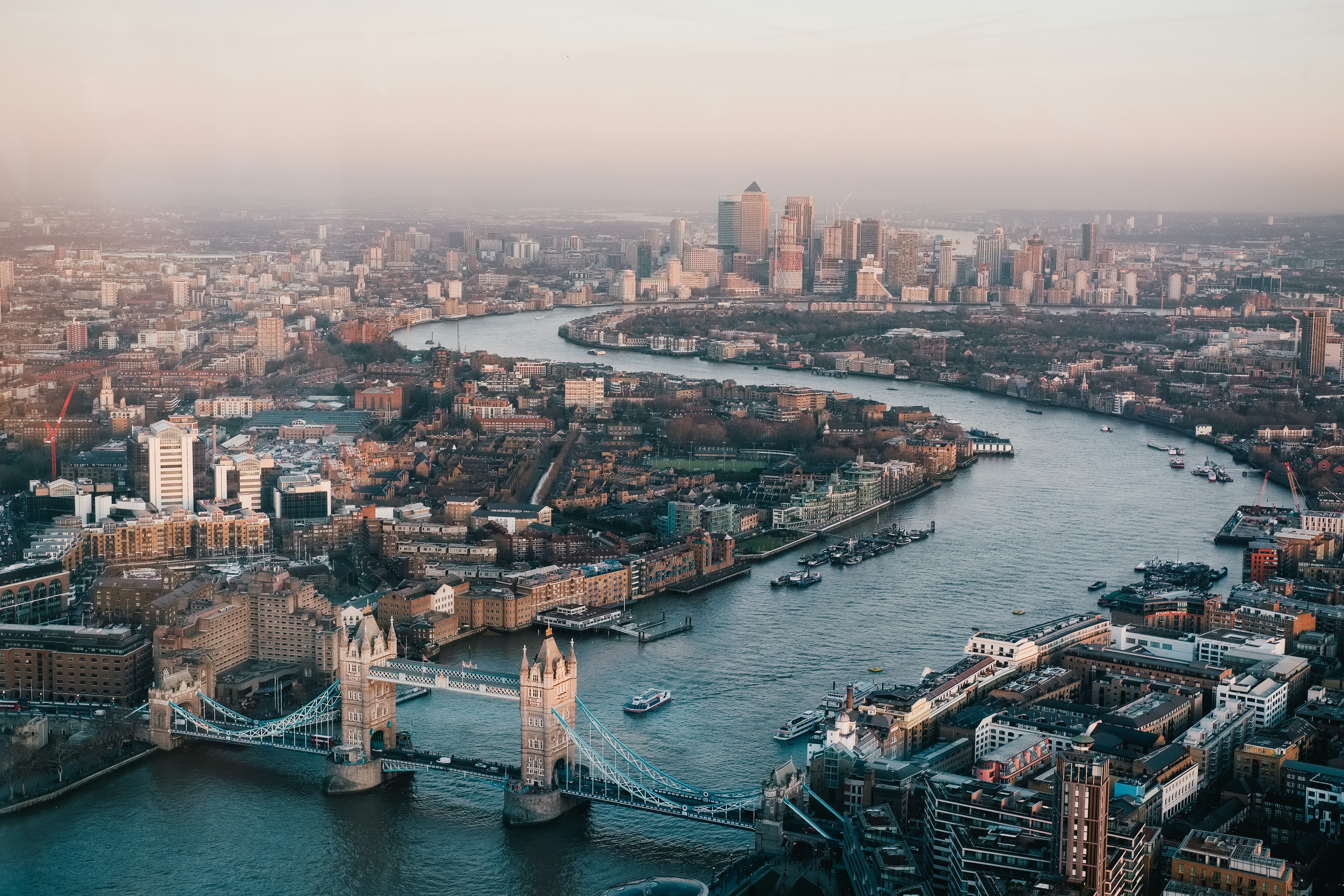 Aerial view of London featuring the winding River Thames, Tower Bridge in the foreground, and modern skyscrapers of Canary Wharf beyond—a stunning scene to inspire your Winter Olympics 2026 Travel Packages.