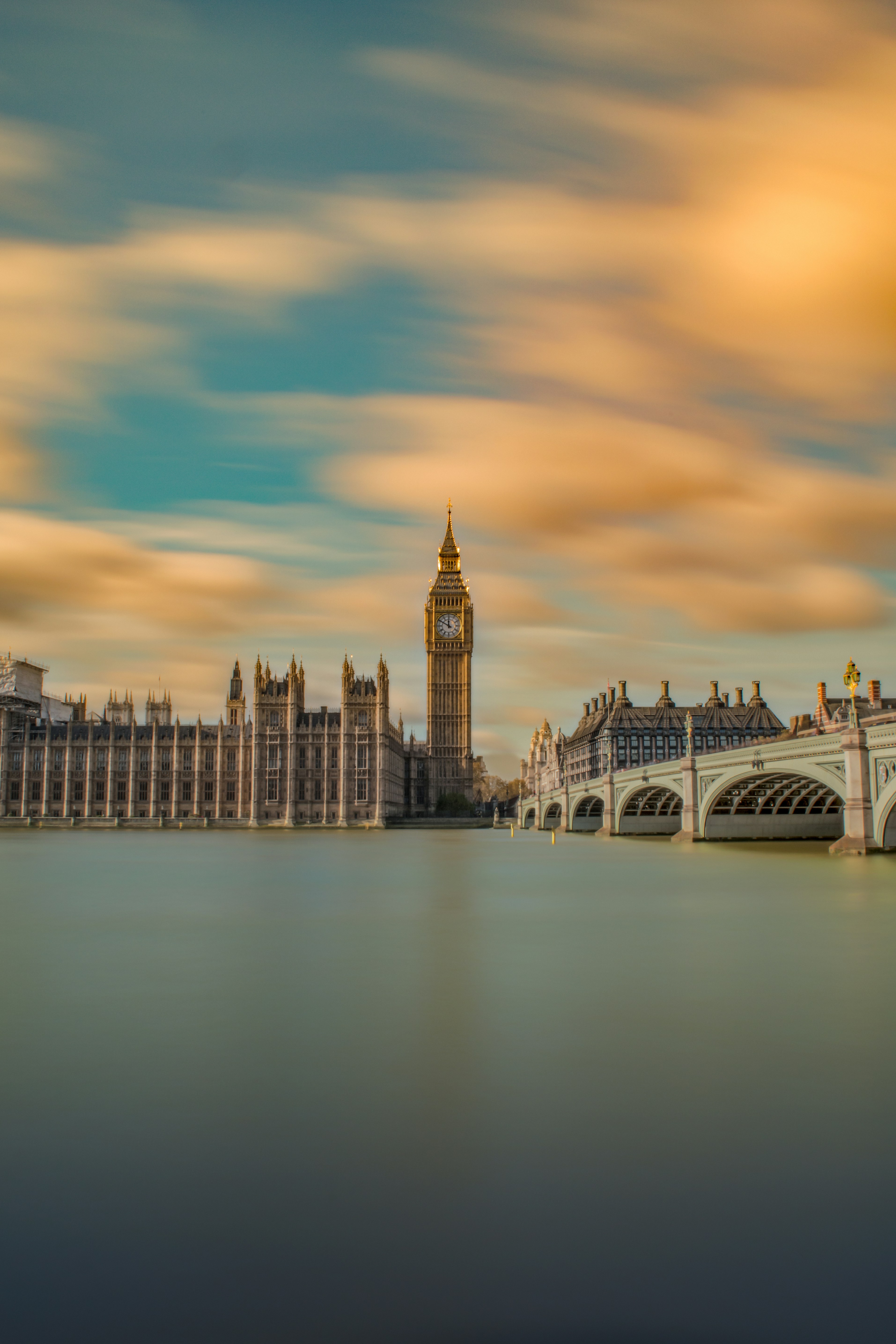Long exposure photo of the Palace of Westminster and Big Ben in London, with blurred clouds in the sky and the smooth River Thames in front—an iconic view easily added to your itinerary with Ryder Cup Ireland 2027 Travel Packages. Westminster Bridge is on the right.