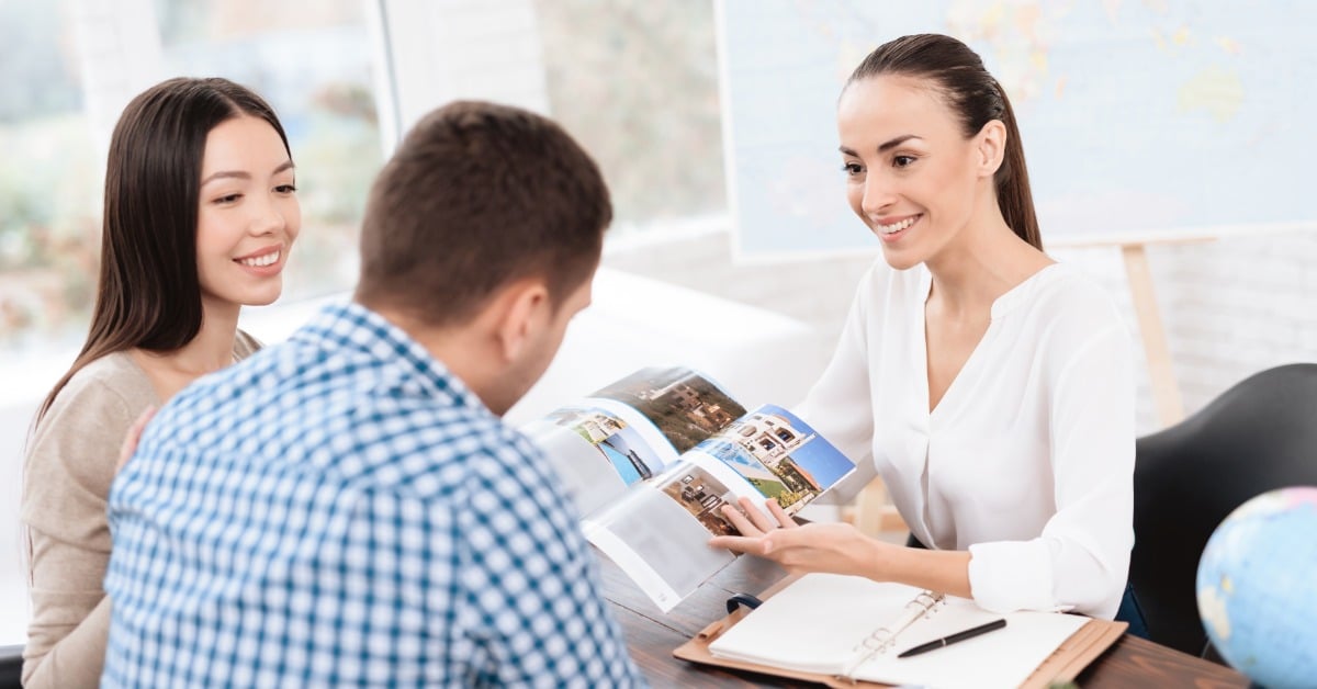 A female travel agent sits across from a couple who is planning a European vacation. She shows them images.
