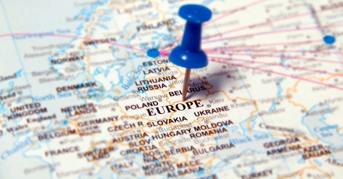 A close-up of a blue push pin stuck in a map. The pin is in the middle of Europe with country names in black ink.