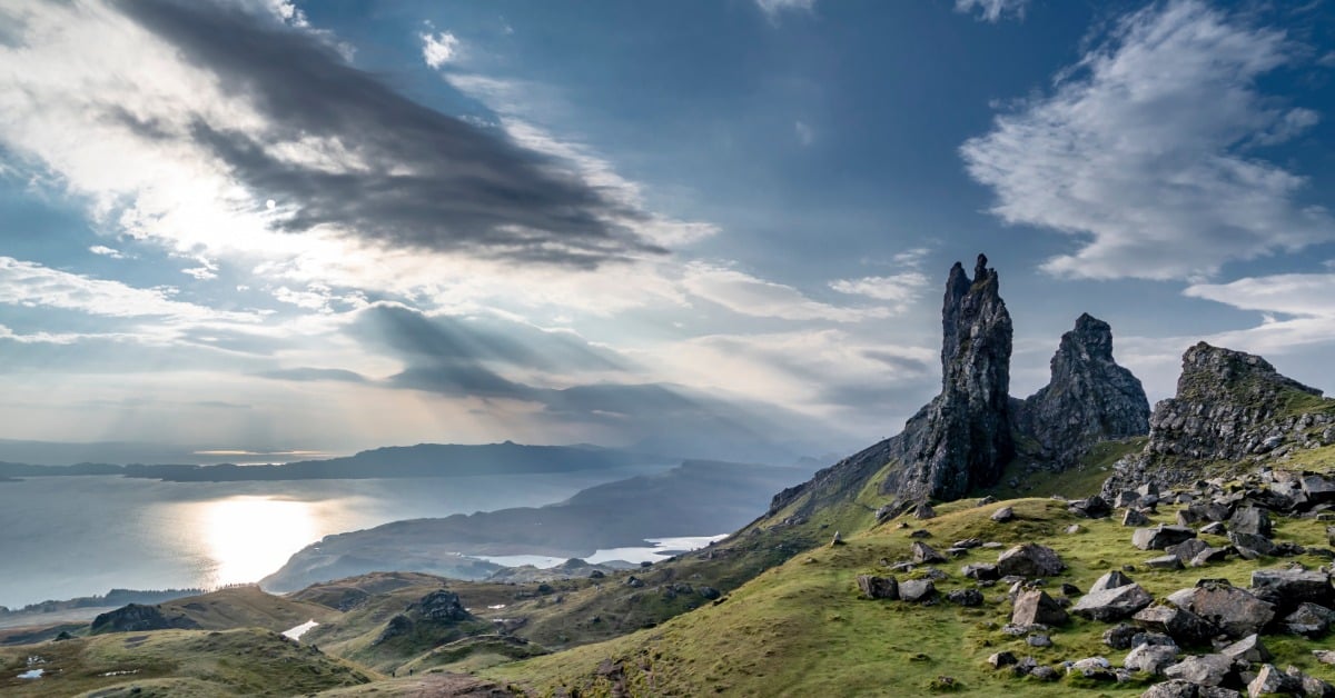 A sunrise view of the Isle of Skye with small clouds and rocks and cliffs at the edge of the water.